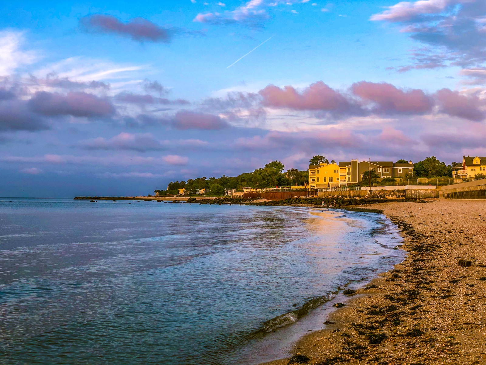 Bayville Beach shoreline at sunrise with pebbly sand, calm water and yellow houses behind