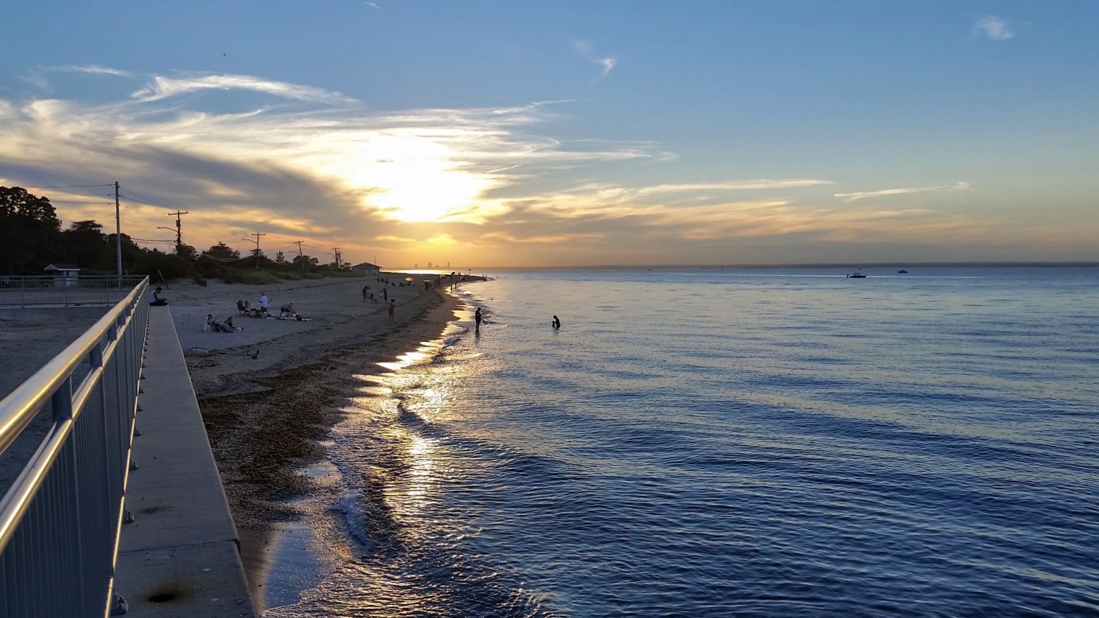 Sandy beach and boardwalk railing along calm water at sunset