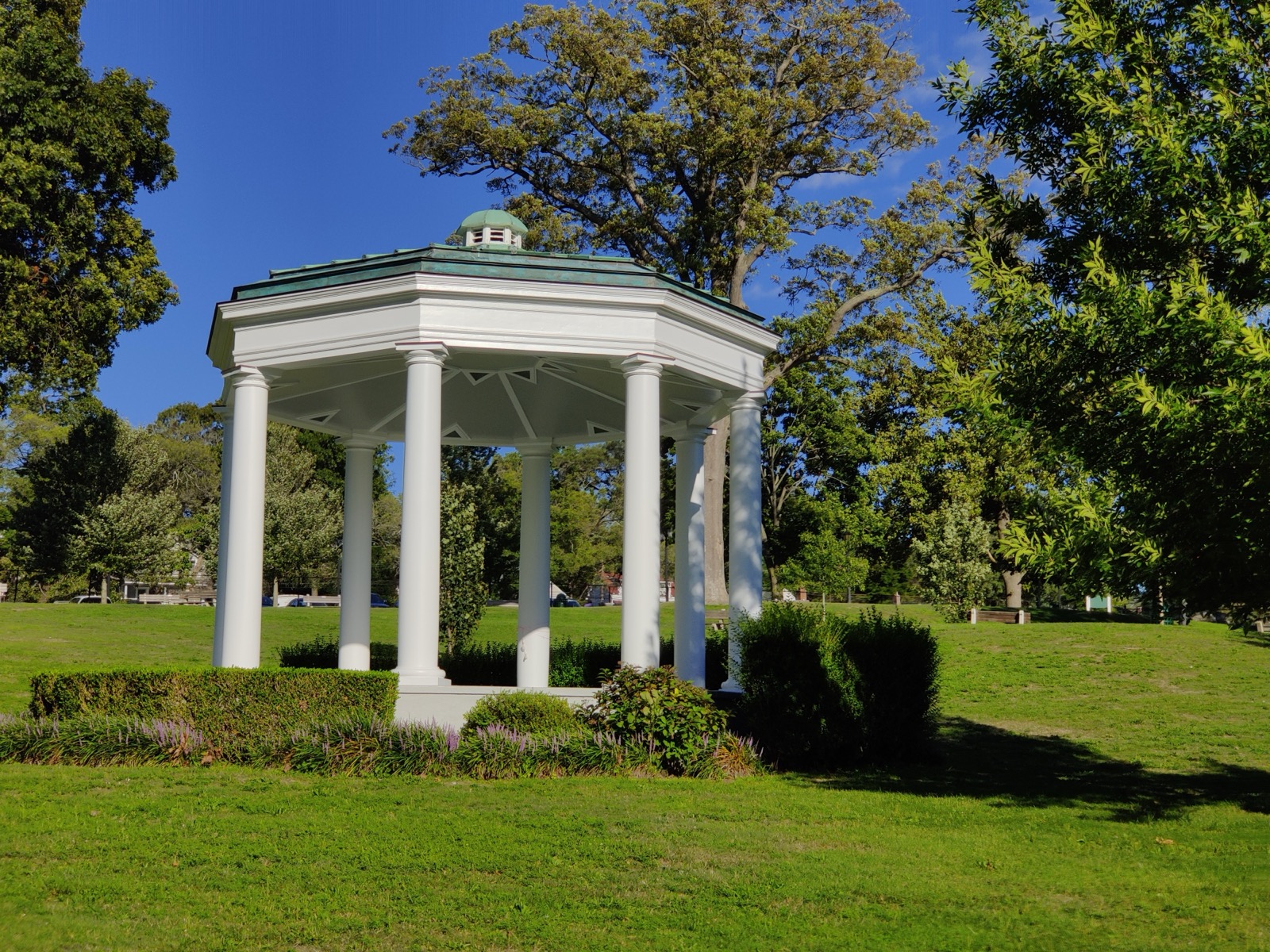 White columned gazebo on a green lawn in Morgan Memorial Park under blue sky