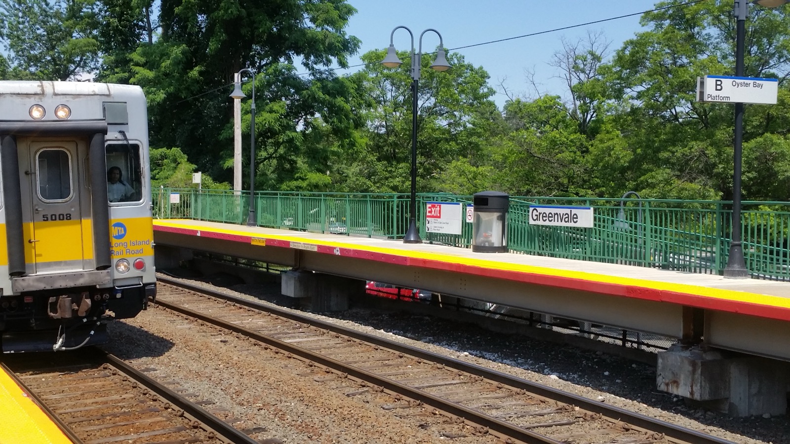 Greenvale LIRR platform sign beside a passing yellow commuter train