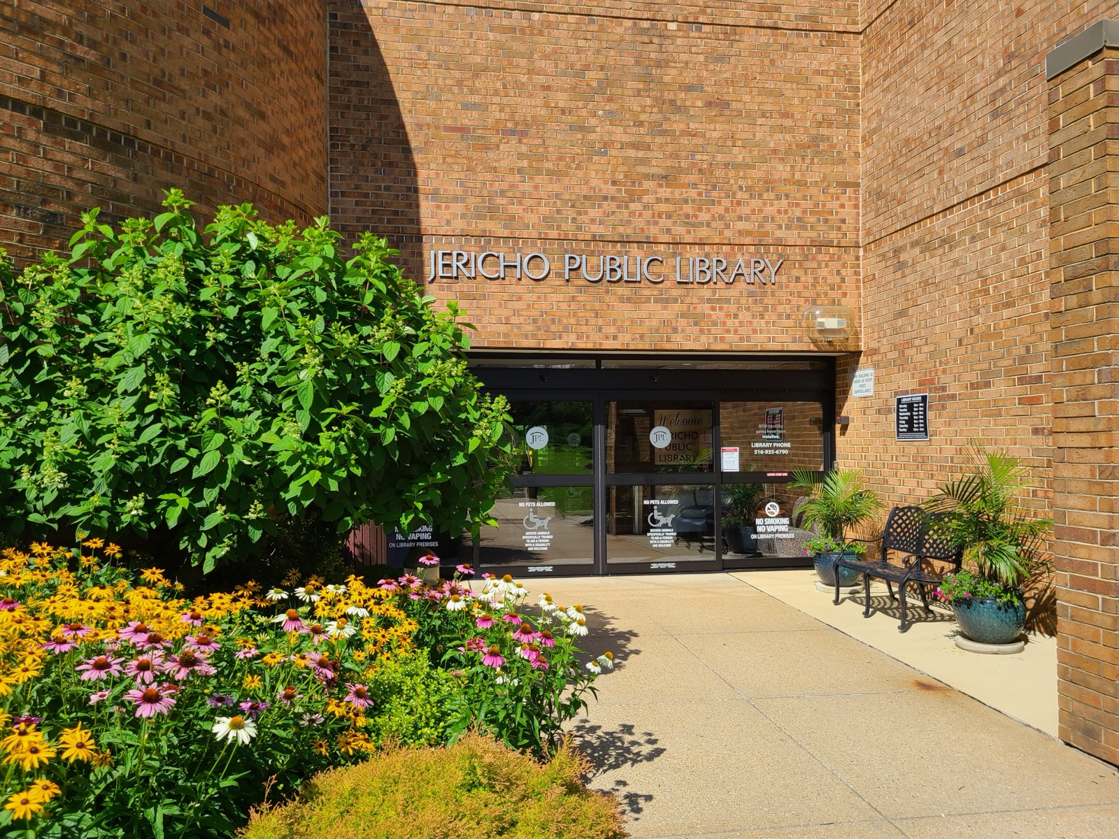 Jericho Public Library brick entrance with flower beds and sign above glass doors