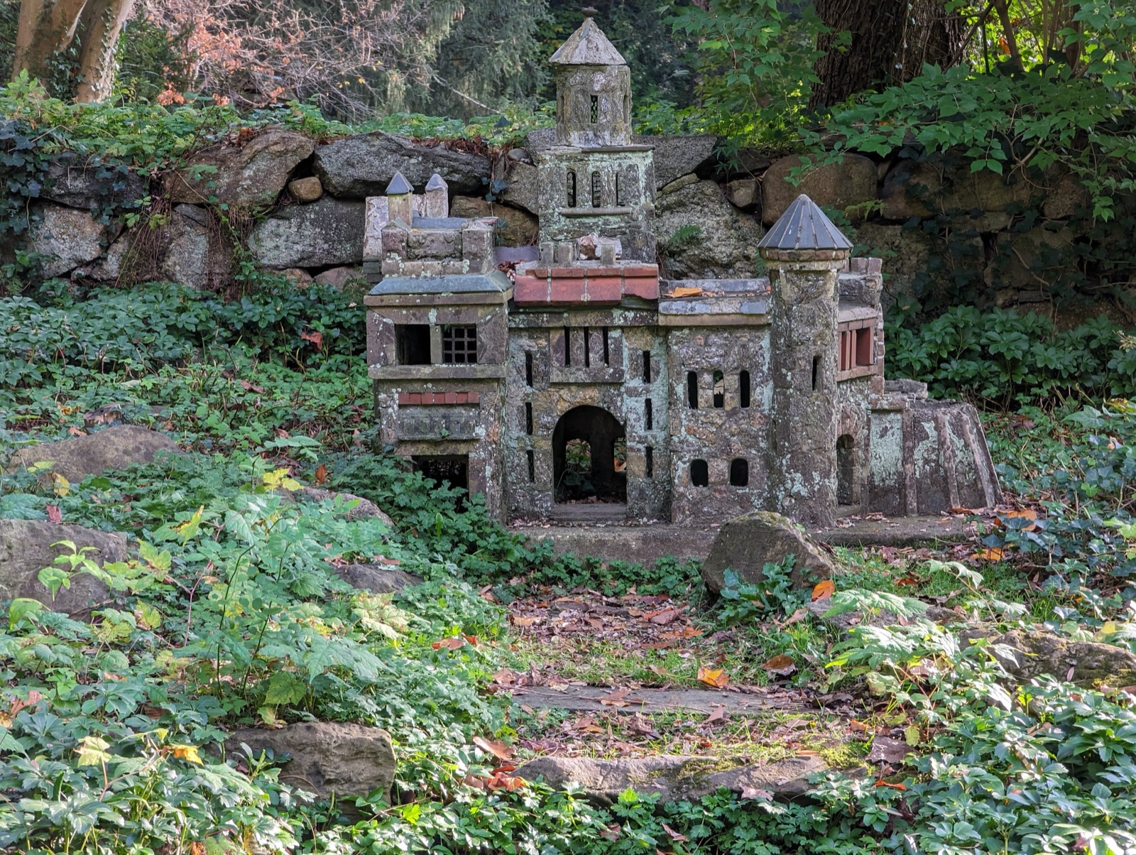 Miniature stone castle model set among ferns and rocks in Bailey Arboretum