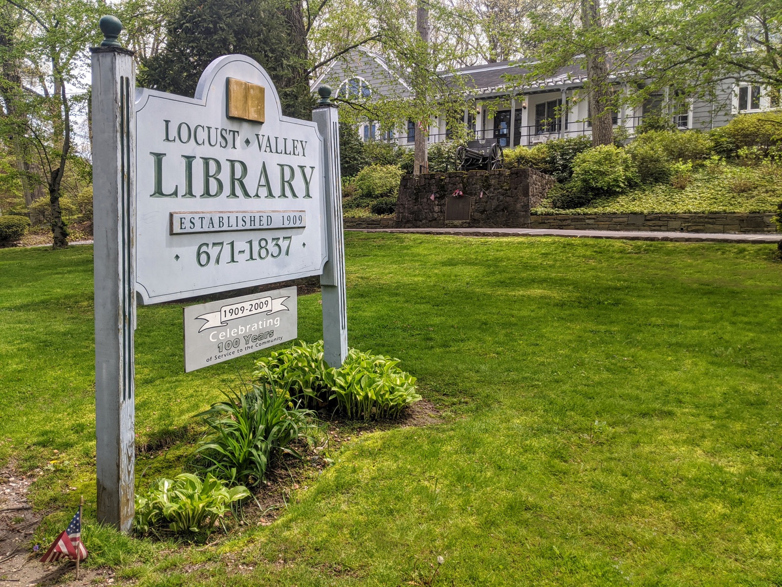 Locust Valley Library entrance sign on a green lawn with a house behind