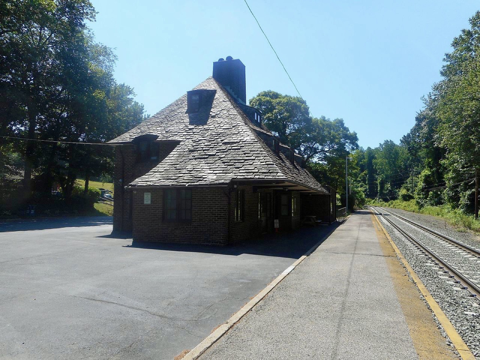 Slate-roofed brick station depot beside a railroad track on a sunny day