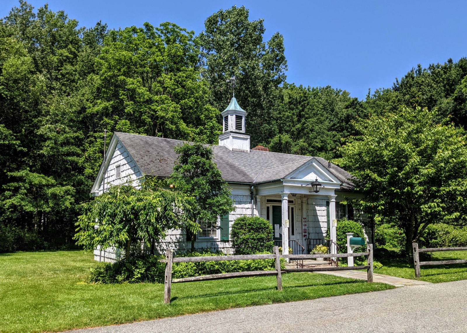 White-clapboard Old Brookville Village Hall cottage with porch and wooden split-rail fence