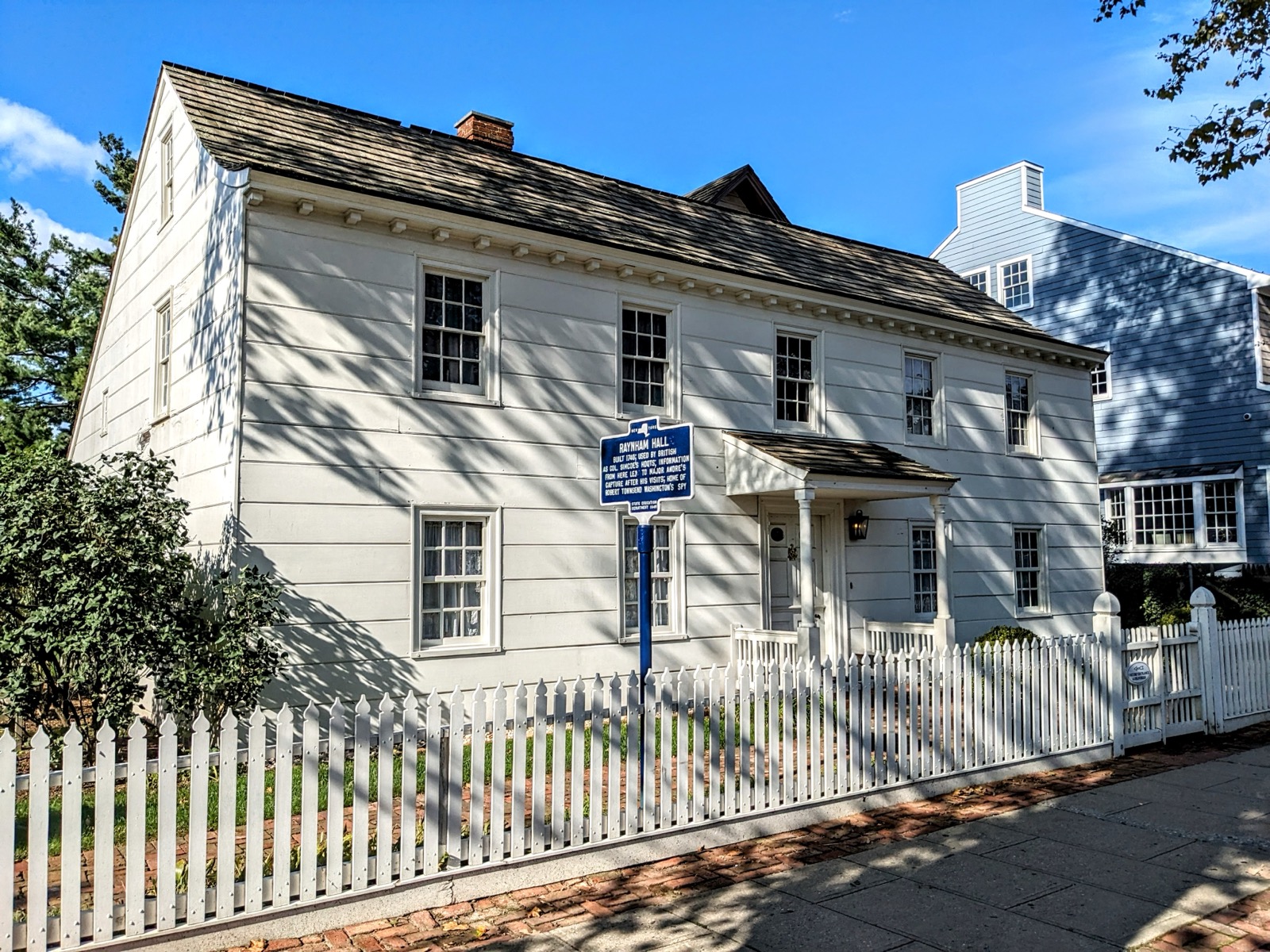 White colonial-style Raynham Hall with blue historic marker and white picket fence