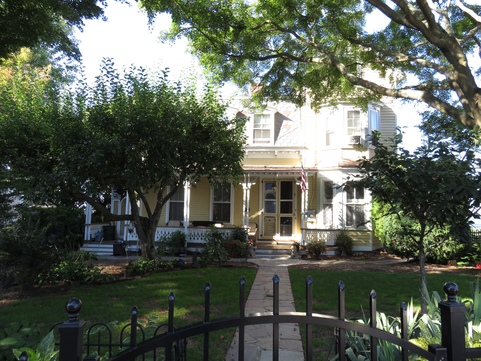 Yellow two-story Victorian house with a front porch, white trim and a flagstone walk behind an iron fence, in Sea Cliff