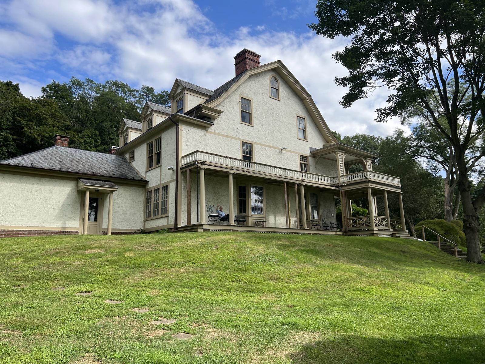 Cream clapboard house with a wide porch and red chimney on a grassy lawn