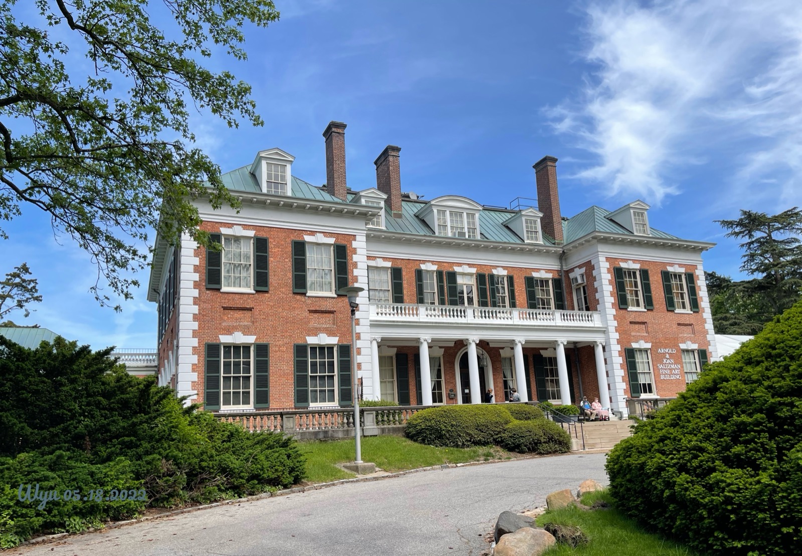 Brick mansion with white columns and a long front porch behind a gravel drive