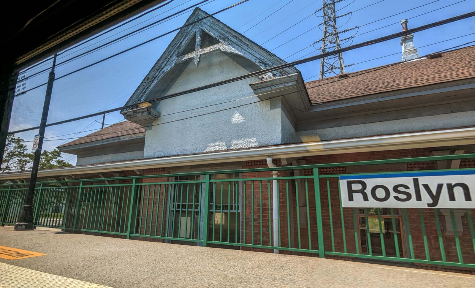 Roslyn LIRR station depot behind a green platform fence with a Roslyn sign