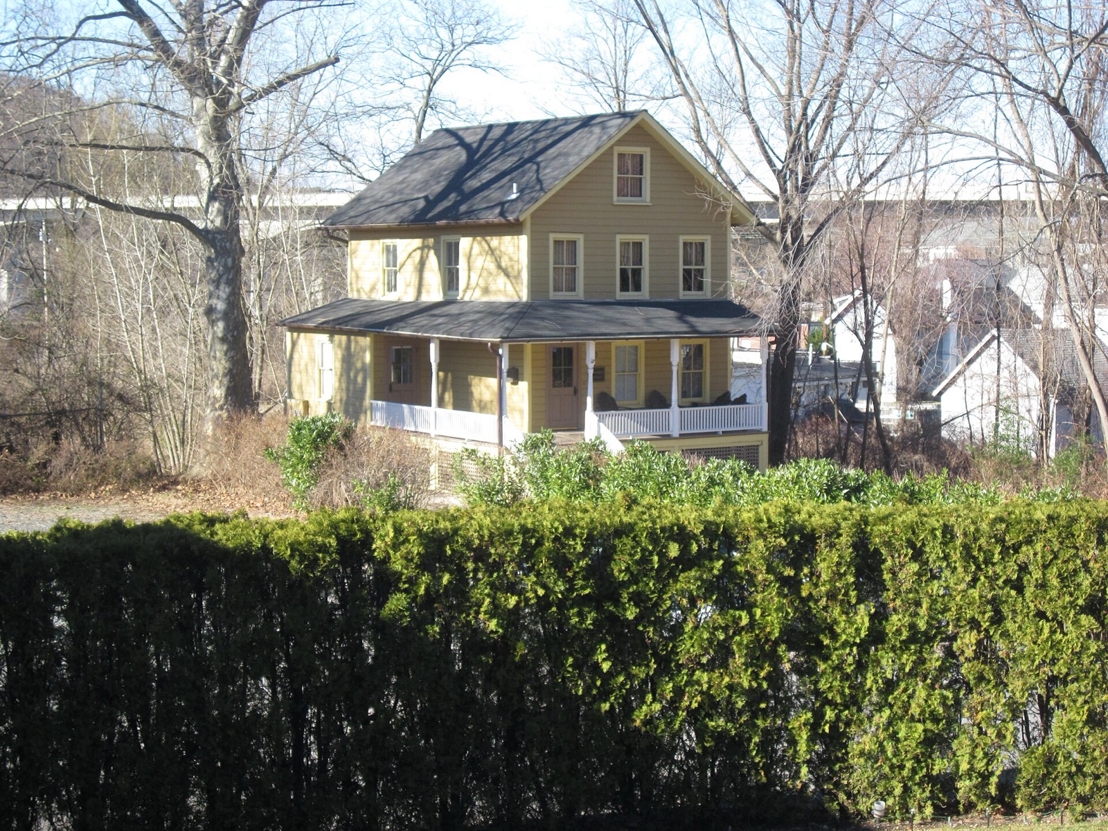 Yellow two-story house with a front porch in Roslyn, behind a tall hedge