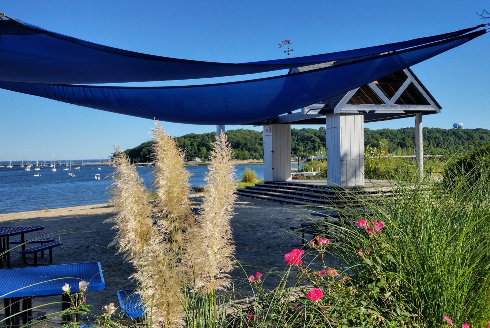 Shade sails and the beach pavilion at Sea Cliff Beach, with moored boats on Hempstead Harbor