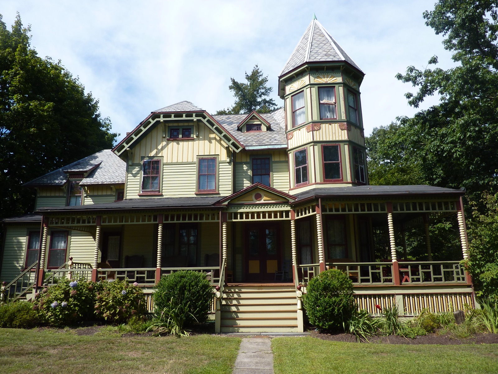 Pale green Victorian house with a corner tower and a wraparound porch, set on a lawn