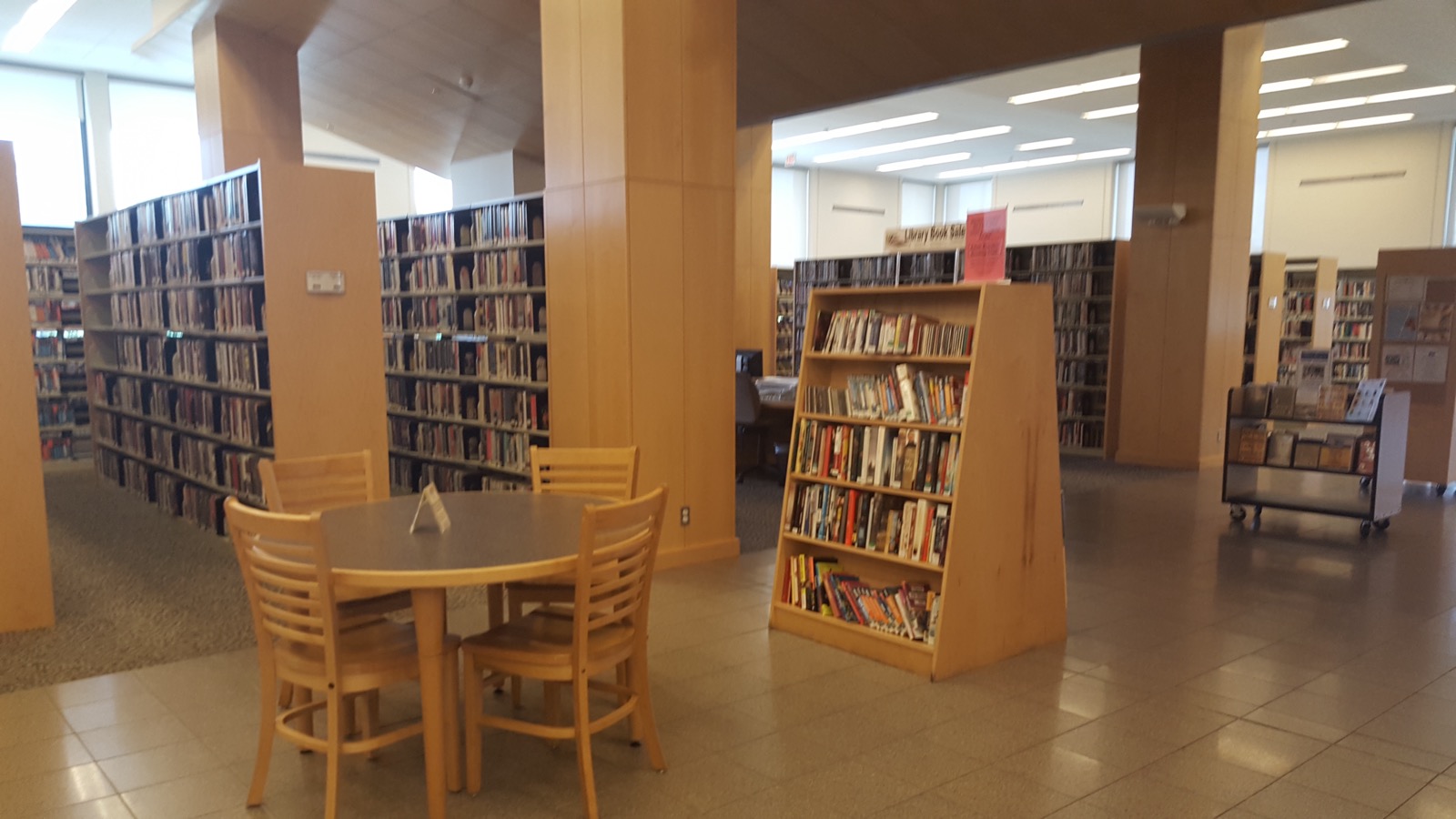 Syosset Public Library reading area with wooden tables, shelves of books and tiled floor