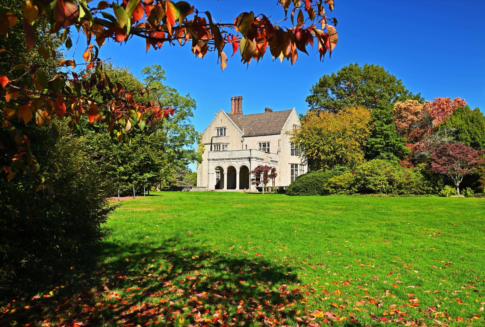 Stone Tudor-style Coe Hall behind a wide green lawn with autumn leaves